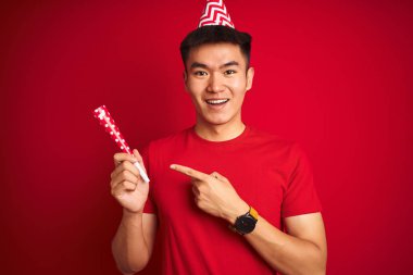 Asya çinli adam doğum günü kutlaması izole kırmızı arka plan üzerinde komik şapka giyen çok mutlu el ve parmak ile işaret