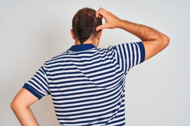Sıradan çizgili polo giyen genç adam izole edilmiş beyaz arka planda dikiliyor. Elleri kafasında şüpheyi düşünüyor.