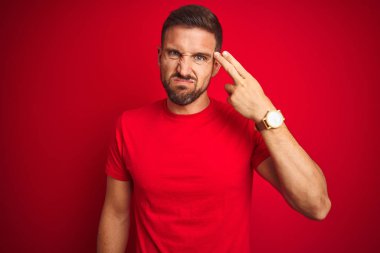 Genç yakışıklı adam kırmızı izole arka plan üzerinde rahat t-shirt giyen Çekim ve kendini silah gibi baş el ve parmakları gösteren öldürme, intihar jesti.
