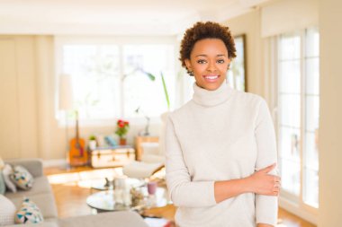 Emin çapraz kolları olan diş gösterilen kameraya gülümseyen güzel genç Afro-Amerikan kadın