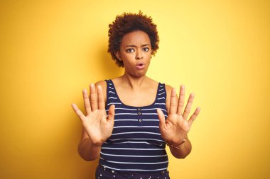 Beauitul afro-amerikan kadın izole sarı arka plan üzerinde yaz t-shirt giyen uzak elleri avuç içi korku ve ifade ile reddetme ve inkar gösteren hareketli. Dur ve yasak.