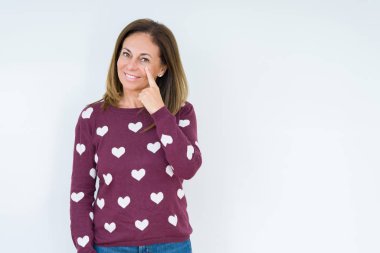 Güzel orta yaşlı bir kadın, izole edilmiş arka planda kalp süveteri giyiyor. Gözünü dikip jestini izliyor. Şüpheli bir ifade.