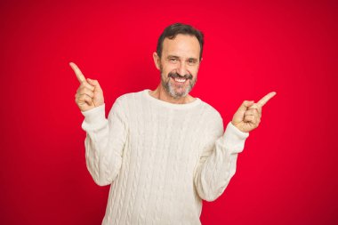 Izole kırmızı arka plan üzerinde gri saçlı yakışıklı orta yaş yaşlı adam farklı yönlere parmakları ile işaret emin gülümseyerek. Reklam için kopya alanı