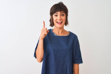Genç güzel kadın başarılı bir fikir ile parmak işaret izole beyaz arka plan üzerinde duran denim elbise giyiyor. Çıktı ve mutlu. Bir numara.