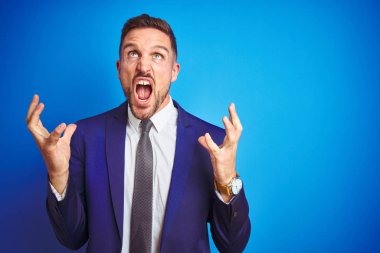 Mavi izole arka plan deli ve deli bağırarak ve agresif ifade ve kollar kaldırdı ile bağırıyor üzerinde genç yakışıklı iş adamı. Hayal kırıklığı kavramı.