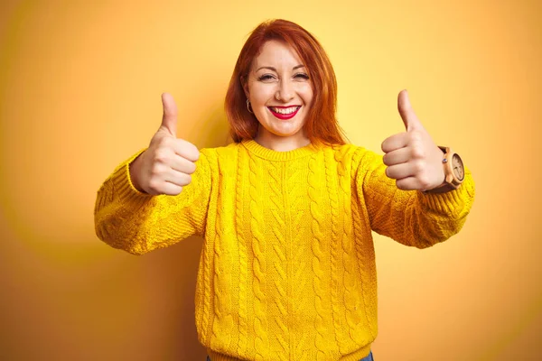 美丽的红头发女人穿着冬季毛衣站在孤立的黄色背景的成功标志上做着积极的手势 微笑着竖起大拇指 快乐地 快乐的表情和胜利的姿态 — 图库照片