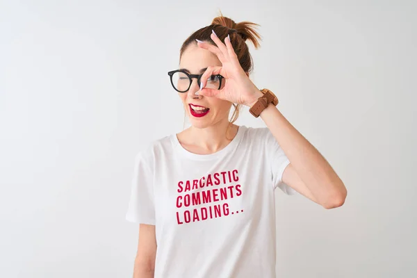 Redhead woman wearing funny t-shirt with irony comments over isolated white background with happy face smiling doing ok sign with hand on eye looking through fingers