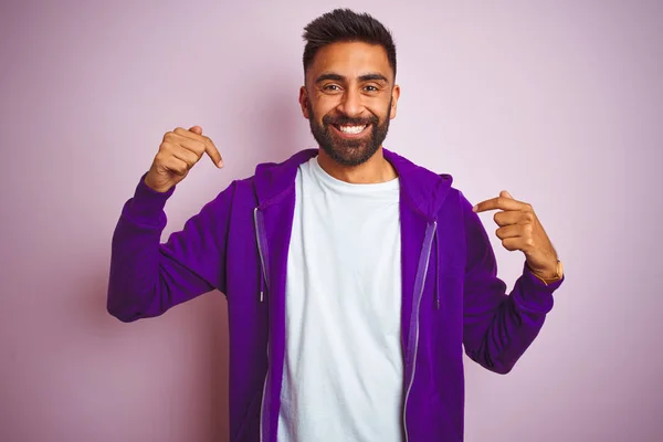 年轻的印度男子穿着紫色运动衫站在孤立的粉红色背景上 面带微笑 面带微笑 用手指指着自己骄傲而快乐 — 图库照片