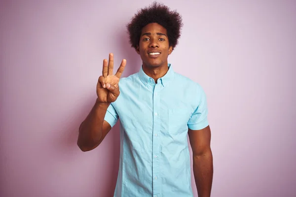 年轻的美国男子与非洲头发穿着蓝色衬衫站在孤立的粉红色背景显示和指向手指三 同时微笑自信和快乐 — 图库照片