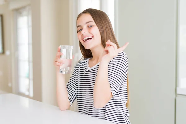 美丽的年轻女孩孩子喝一杯新鲜的水很高兴指着手和手指的一边 — 图库照片