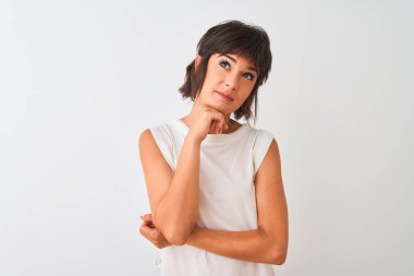 Genç güzel kadın gündelik t-shirt giyen çene üzerinde el ile izole beyaz arka plan üzerinde duran soru, dalgın ifade düşünme. Düşünceli bir yüzle gülümsüyor. Şüphe kavramı.