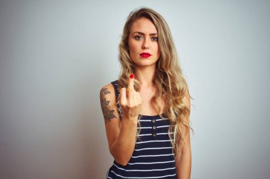 Çizgili tişört giyen genç ve güzel bir kadın beyaz tenli arka planda duruyor orta parmağını gösteriyor, kaba ve kaba bir ifade takınıyor.