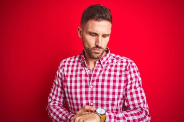 Kırmızı izole arka plan üzerinde genç yakışıklı adam kol saati, rahat ve kendinden emin zaman kontrol