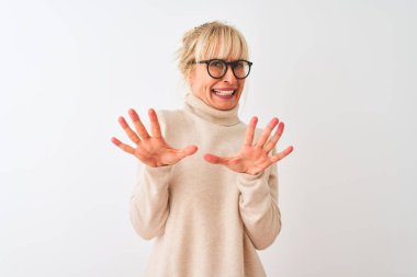 Orta yaş kadın boğazlı kazak ve gözlük giyen izole beyaz arka plan üzerinde korkmuş ve korku ifade ile korkmuş elleriyle jest durdurmak, şok içinde bağırarak. Panik kavramı.