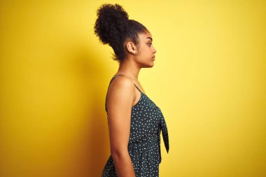 Izole sarı arka plan üzerinde yaz rahat yeşil elbise giyen Afrikalı-Amerikalı kadın yan bakarak, kendine güvenen gülümseme ile doğal yüzü ile profil poz rahat.