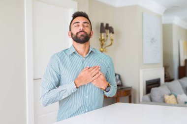 Evde yakışıklı İspanyol adam kapalı gözler ve yüz minnettar jest ile göğsünde eller ile gülümsüyor. Sağlık konsepti.
