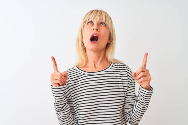 Izole beyaz arka plan üzerinde duran lacivert çizgili t-shirt giyen orta yaş kadın şaşırttı ve yukarı bakarak ve parmakları ile işaret ve kolları kaldırdı şaşırttı.