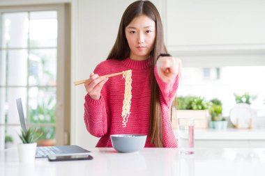 Güzel Asyalı kadın dizüstü bilgisayar kullanarak çalışan ve kamera ve size parmak ile işaret asya erişte yeme, el işareti, önden olumlu ve kendinden emin jest