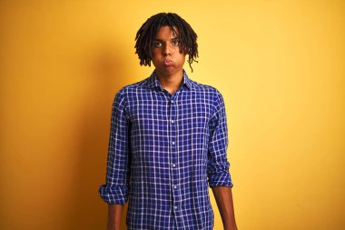 Komik yüzü ile izole sarı arka plan üzerinde duran rahat gömlek giyen dreadlocks ile Afro adam yanakları şişirme. Ağız hava ile şişirilmiş, deli ifade.