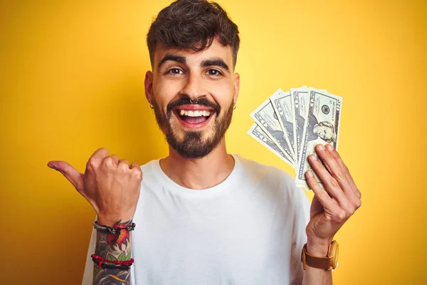 Young Man Tattoo Holding Dollars Standing Isolated Yellow Background Pointing — Stock Photo, Image