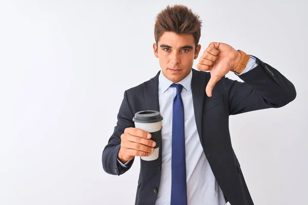 Young handsome businessman wearing suit holding coffee over isolated white background with angry face, negative sign showing dislike with thumbs down, rejection concept