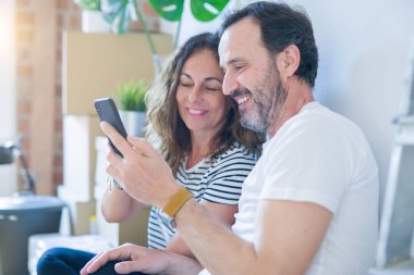 Orta yaş üst düzey romantik çift aşk etrafında kutuları ile daire katında oturan ve akıllı telefon yeni bir eve taşımak için mutlu gülümseyen kullanarak