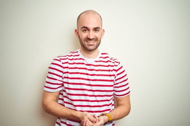 Young bald man with beard wearing casual striped red t-shirt over white isolated background with hands together and crossed fingers smiling relaxed and cheerful. Success and optimistic