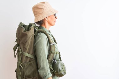 Orta yaş yürüyüşçü kadın izole beyaz arka plan üzerinde sırt çantası kantin şapka gözlük giyen yan bakarak, kendine güvenen gülümseme ile doğal yüz ile profil poz rahatla.