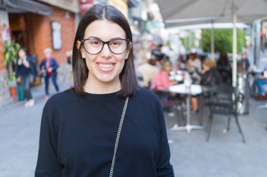 Şehir sokaklarında yürürken heyecanlı gülümseyen güzel genç esmer kadın, şehirde açık havada mutlu ve güven ifade ayakta