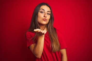 Genç güzel kadın izole kırmızı arka plan üzerinde duran t-shirt giyen kamera hava güzel ve seksi olmak el iyle bir öpücük üfleme bakarak. Aşk ifadesi.