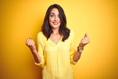 Sarı arka planda duran zarif kadın kollarını kaldırarak ve açık gözlerle başarının şaşkınlığını ve şaşkınlığını kutluyor. Kazanan konsept.