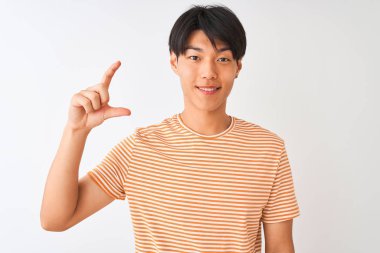 Izole beyaz arka plan üzerinde duran rahat çizgili t-shirt giyen genç Çinli adam gülümseyerek ve el parmakları görünümlü ve kamera ile küçük boyutlu işareti yapıyor emin gesturing. Ölçü kavramı.