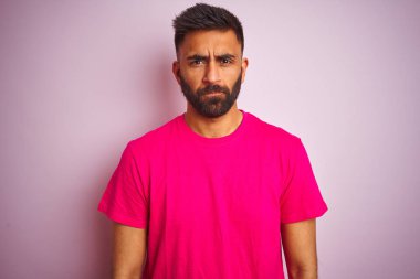 Genç hintli adam izole pembe arka plan şüpheci ve sinir üzerinde duran t-shirt giyen, sorun nedeniyle üzgün kaşlarını çatma. Negatif kişi.