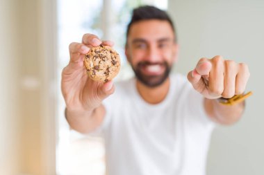 Yakışıklı İspanyol adam kameraya parmak la işaret çikolata parçaları çerezleri yeme ve size, el işareti, önden olumlu ve kendinden emin jest