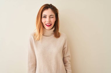 Seksi ifade, neşeli ve mutlu yüz ile kameraya bakarak izole beyaz arka plan göz kırpma üzerinde duran zarif boğazlı kazak giyen Redhead kadın.