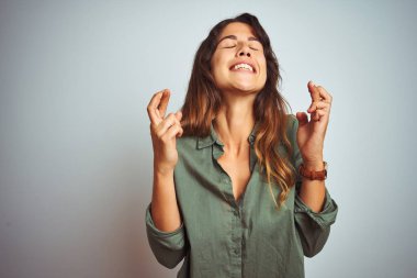 Yeşil tişörtlü genç bir kadın gri izole edilmiş arka planda duruyor. Umut ve gözler kapalı bir şekilde gülümseyerek işaret ediyor. Şans ve batıl inanç..