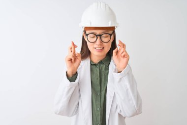 İzole beyaz arka plan gesturing parmak üzerinde ceket kask gözlük takan genç Çinli mühendis kadın umut ve gözleri kapalı gülümseyerek geçti. Şans ve batıl kavram.