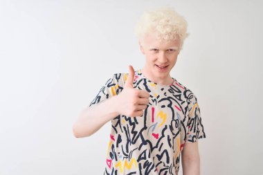 Genç albino sarışın adam renkli t-shirt izole beyaz arka plan üzerinde el ile jest kadar mutlu başparmak yapıyor ayakta giyiyor. Başarı göstererek kameraya bakan ifadeyi onaylama.