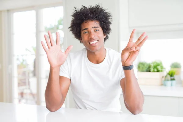 カジュアルな白いTシャツを着た若いアフリカ系アメリカ人男性が 自信を持って幸せに微笑みながら 8番の指を見せ 指を上げている — ストック写真