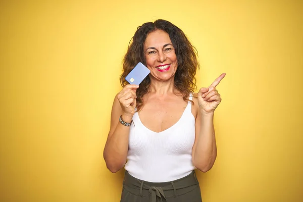 Seniorin Mittleren Alters Hält Kreditkarte Über Gelbem Hintergrund Und Zeigt — Stockfoto