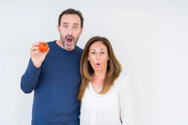 驚きの顔でショックを受け 恐怖表現で興奮した孤立した背景の上に新鮮なトマトを食べる中年のカップル — ストック写真