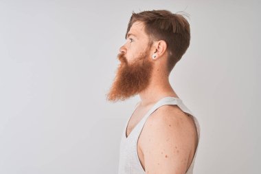 Genç kızıl saçlı İrlandalı adam yan bakarak izole gri arka plan üzerinde duran t-shirt giyen, kendine güvenen gülümseme ile doğal yüzü ile profil poz dinlenmek.