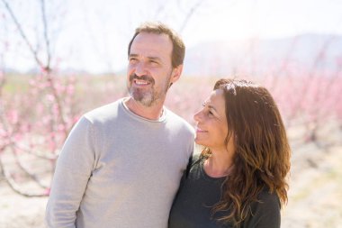 Baharın güneşli bir gününde pembe yaprakları ile şeftali ağaçlarının romantik bahçesinde aşık gülümseyen güzel orta yaş yaşlı çift