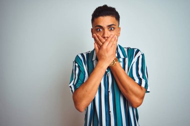 İzole beyaz arka plan üzerinde duran yazlık çizgili gömlek giyen brezilyalı genç adam hata için elleri ile ağız kapsayan şok. Gizli kavram.