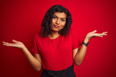 Güzel transseksüel transseksüel kadın izole kırmızı arka plan üzerinde t-shirt giyen habersiz ve kollar ve eller kaldırdı ile karışık ifade. Şüphe kavramı.