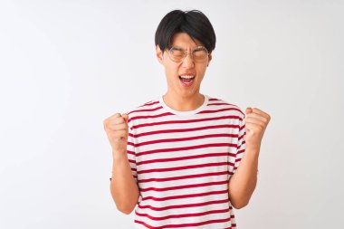 Gözlük takan ve çizgili tişört giyen genç adam izole beyaz arka plan üzerinde ayakta kollarını kaldırdı ve gözleri gülümseyerek zafer kutluyor kapalı başarı için heyecanlı. Kazanan kavramı.