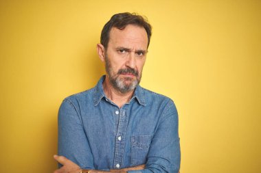Izole sarı arka plan şüpheci ve sinir üzerinde gri saçlı Yakışıklı orta yaş yaşlı adam, çapraz kolları ile yüzünde onaylamayan ifade. Negatif kişi.