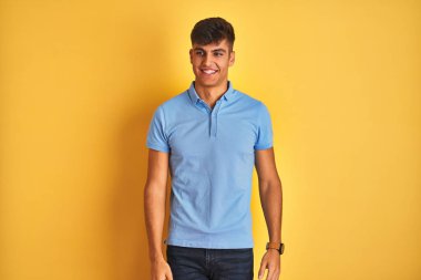 Mavi polo giyen genç hintli adam izole sarı arka plan üzerinde duran yüzünde gülümseme, doğal ifade ile yan bakıyor. Gülmekten emin.