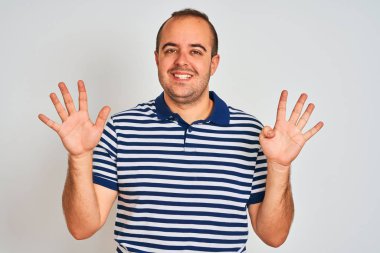 Sıradan çizgili polo giyen genç adam izole edilmiş beyaz arka planda duruyor ve dokuz numaralı parmaklarıyla işaret ederken kendinden emin ve mutlu bir şekilde gülümsüyor..