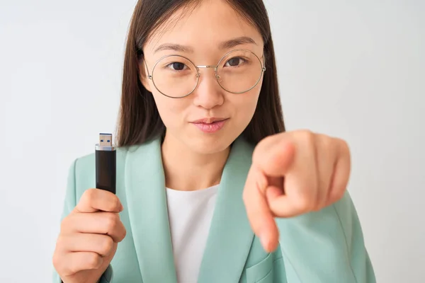 Young chinese businesswoman holding usb memory over isolated white background pointing with finger to the camera and to you, hand sign, positive and confident gesture from the front